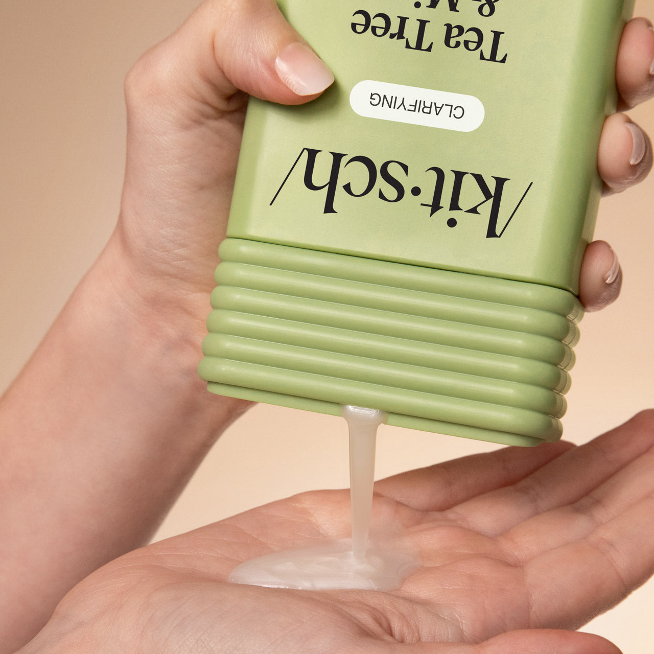 Hand dispensing KITSCH Clarifying Tea Tree & Mint Shampoo from bottle into palm on a beige background