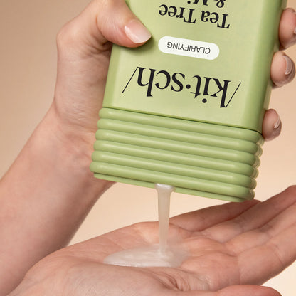 Hand dispensing KITSCH Clarifying Tea Tree & Mint Shampoo from bottle into palm on a beige background
