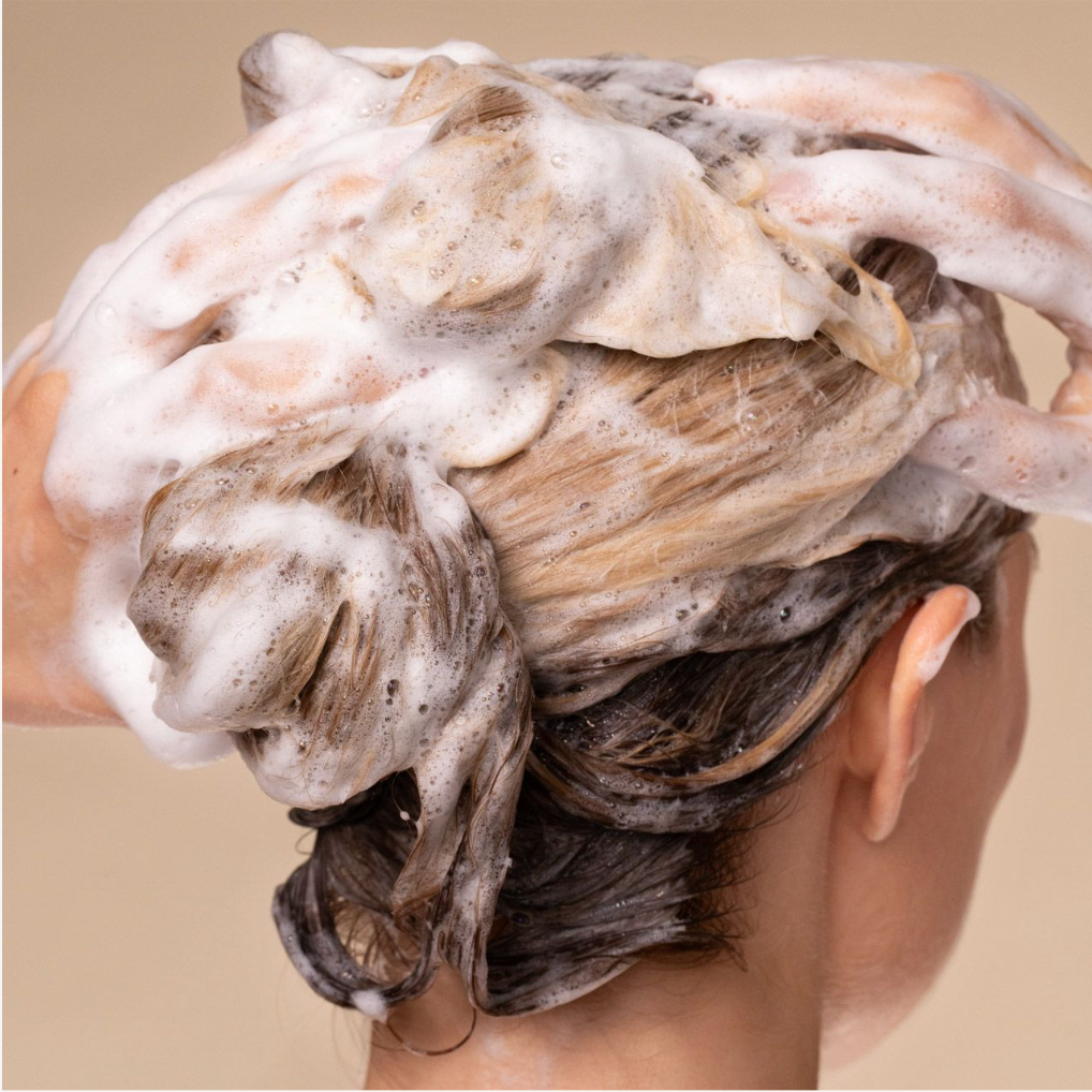 Close-up of model washing hair from behind with KITSCH Repairing Argan Oil Shampoo — rich foam lather visible as hands massage shampoo through hair — lifestyle in-use shot for damaged, weak, & brittle hair formula with Terabond™ & Hydrolyzed Oat Protein